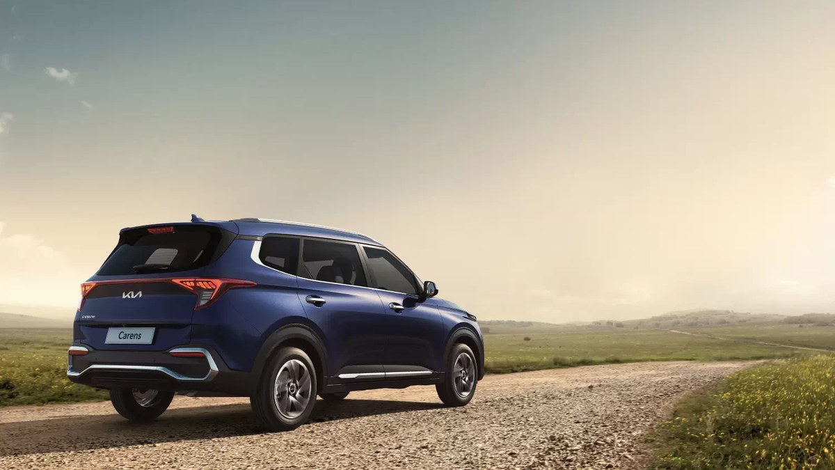 Kia Carens màu xanh nhìn từ phía sau trên đường quê