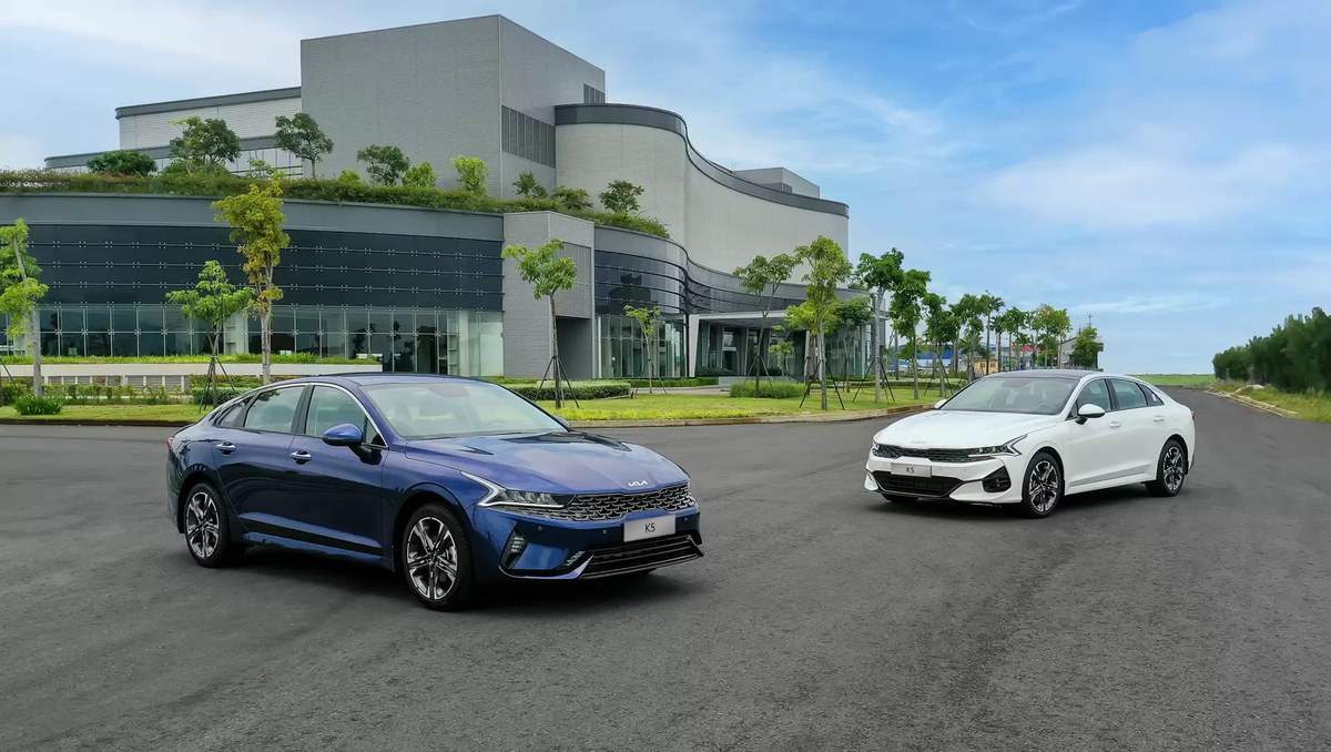 Hai chiếc Kia K5 màu xanh và trắng đỗ trước tòa nhà